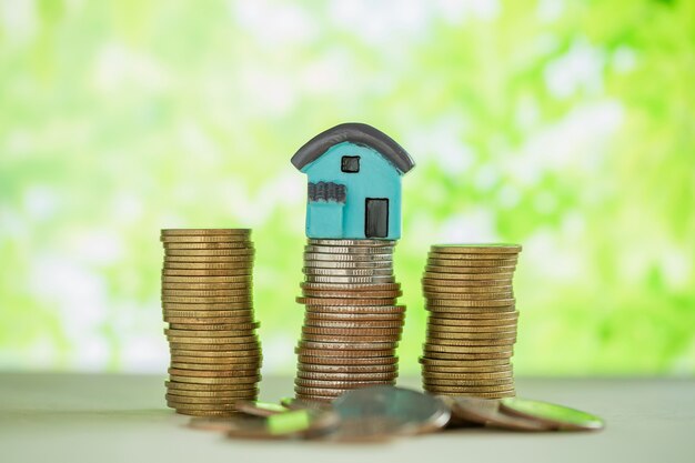 Mini house on stack of coins with green blur. 