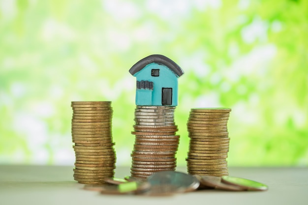 Mini house on stack of coins with green blur. 