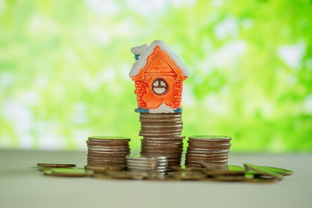 Mini house on stack of coins with green blur. 