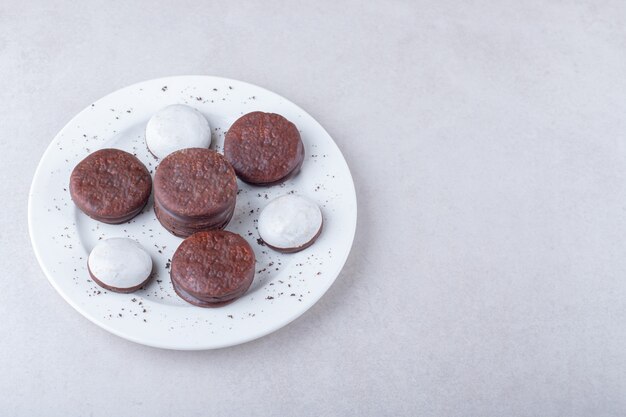 Mini mousse pastry and chocolate coated cookie dessert on a plate, on the dark surface