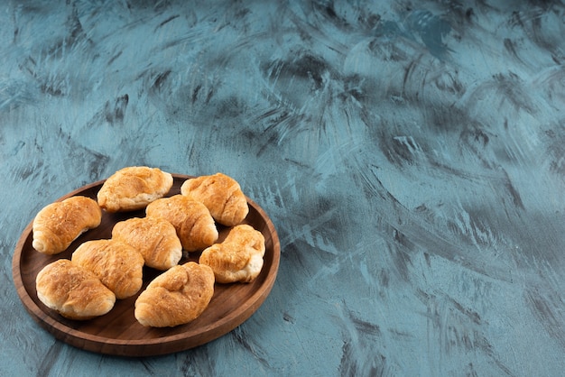 Mini croissant dolci in un piatto di legno su sfondo blu scuro.