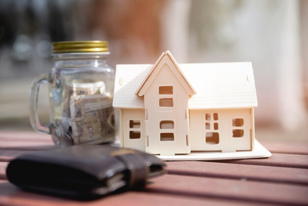 Miniature house with savings jar and wallet