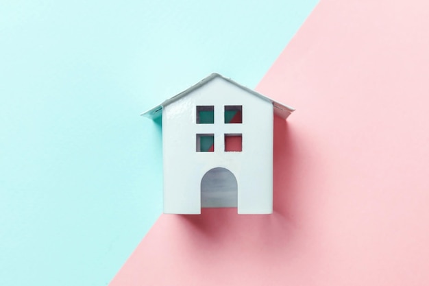 Miniature white toy house on blue and pink pastel background