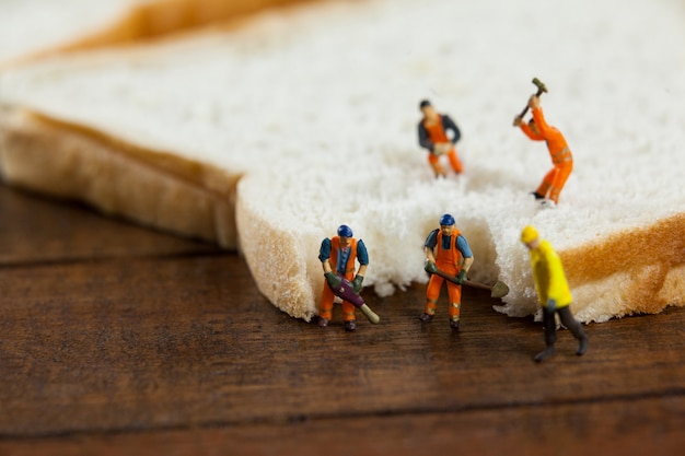 Miniature workers working on sliced of bread