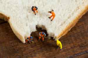 Free photo miniature workers working on sliced of bread