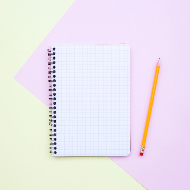 Free photo minimal flat lay composition with empty notebook with pencil on yellow and pink background