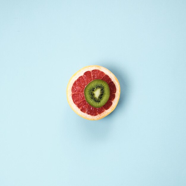 最小限の果物の背景青いテーブルにスライスした柑橘系の果物グレープフルーツとキウイの上面図平面図フラットレイ