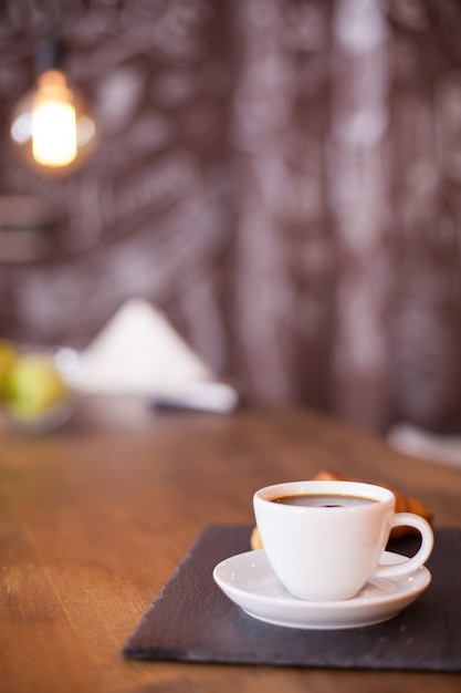 Minimalist composition of a cup of coffee on a black stone plate with blurred background. Tasty coffee. Vintage pub.