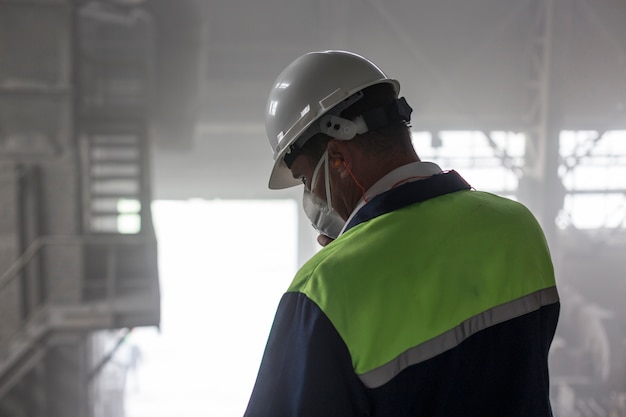 Горный инженер в белом шлеме и респираторе осматривает пыльную грязную мастерскую Premium Фотографии