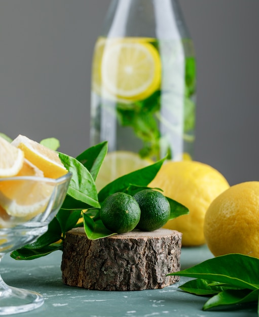 Mint citrus water with lemon leaves, wooden board in a bottle on plaster and grey surface