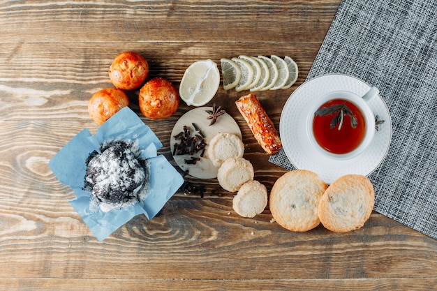 Minty tea in a cup with sliced lemon, biscuits, cloves top view on wooden table