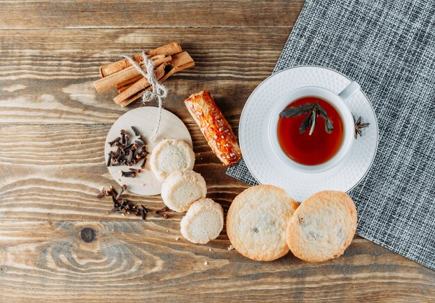 Мятный чай с палочками корицы, печеньем, гвоздикой в чашке на деревянной поверхности