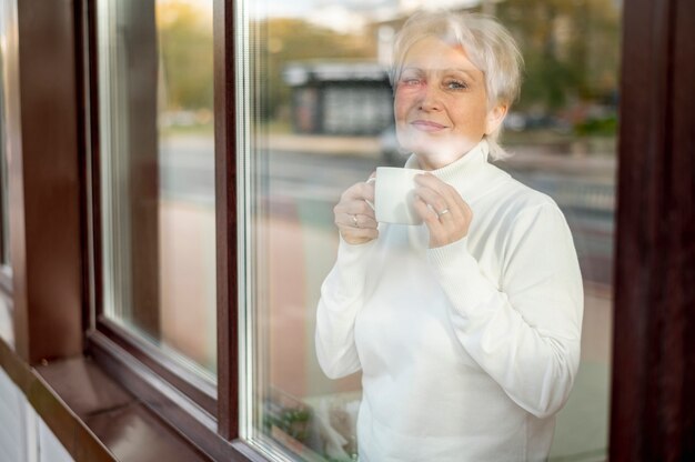 Зеркальное отражение старшего женского пьющего кофе