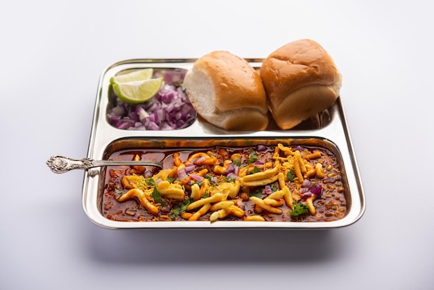 Misal pav is a popular maharashtrian street food of usal, sprouts curry, topped with onions, tomatoes, farsan and chutney Premium Photo