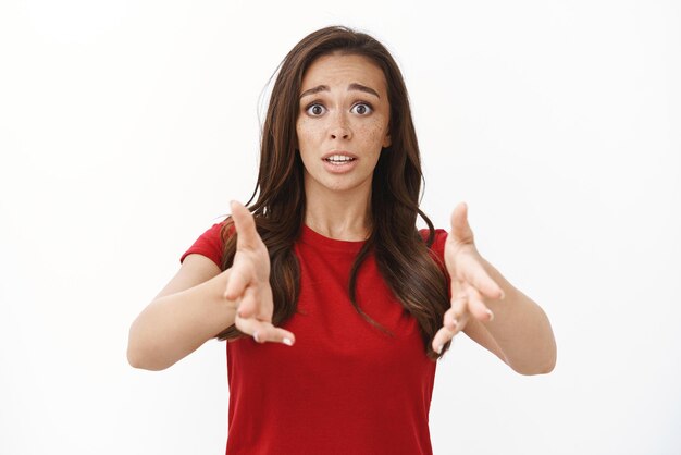 Miserable upset cute timid brunette girl in red tshirt raising hands up in regret and sorrow watching favorite team losing competition looking hopeless and pensive standing white background