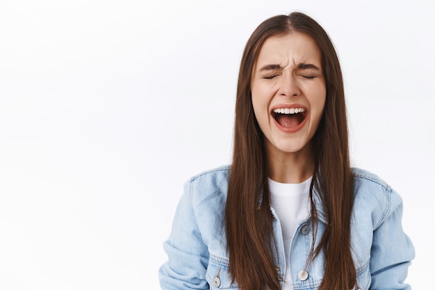 Miserbale upset and depressed pretty brunette girl, crying her heart out, close eyes and screaming unhappy, complaining on cruel unfair life, standing offended and heartbroken, white background