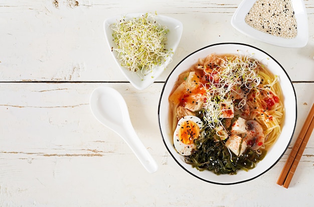 Miso Ramen Asian noodles with cabbage kimchi, seaweed, egg, mushrooms and cheese tofu in bowl on white wooden table. 