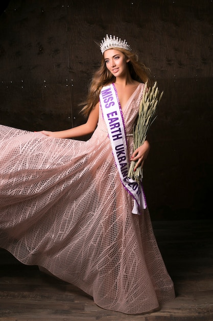 Miss Earth woman wearing the crown, ribbon and spikelets of wheat. Fashion contest, beautiful model posing