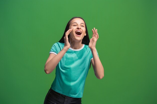 Do not miss. Young casual woman shouting. Shout. Crying emotional woman screaming on green studio background. Female half-length portrait. Human emotions, facial expression concept. Trendy colors