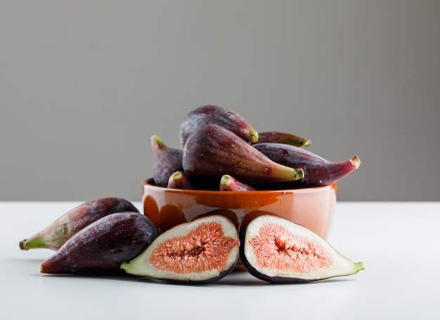 Mission figs in a bowl on a white table with dark background. side view. space for text