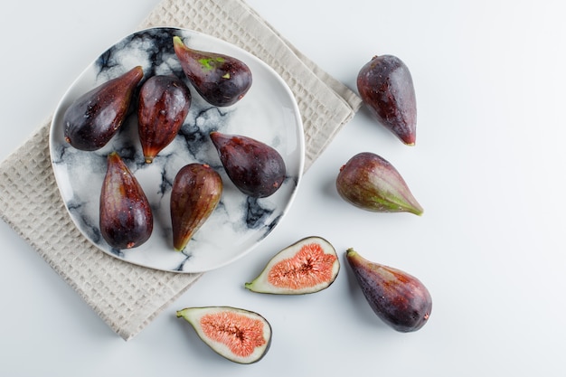 Mission figs and halves in a plate on a cloth and white wall. top view.