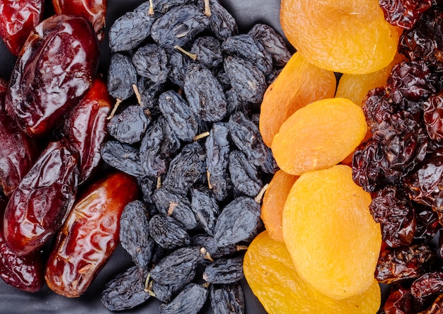 Mix of dried fruits dates black raisins apricots and cherries on black background top view