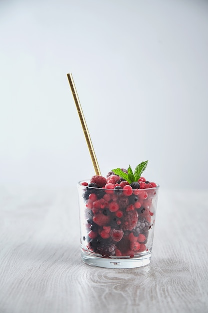 Mix of frozen berries in whiskey rox glass with golden drinking straw inside. Preparation of healthy milky smoothie process