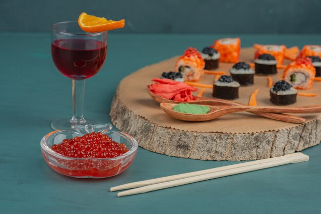 Mix sushi, red caviar and glass of red wine on blue table.