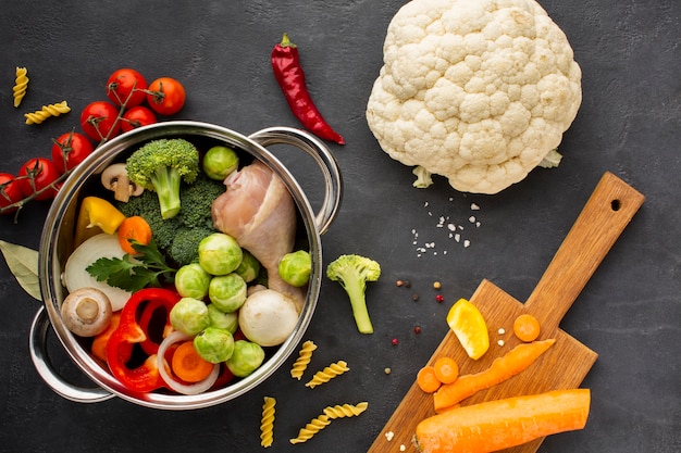 Free photo mix of vegetables and chicken drumstick in pan with carrot on cutting board and cauliflower