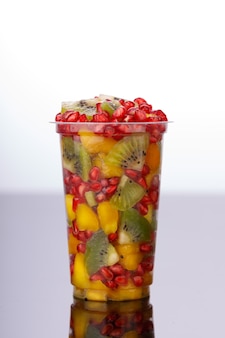 Смешанные фрукты разрезанные в прозрачном стакане с белым фоном, изолированные.