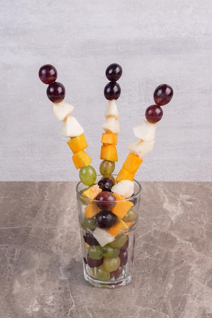 Free photo mixed fruit sticks in glass on marble table.