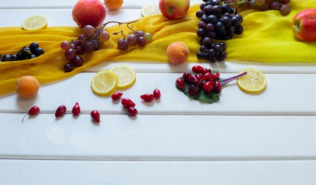 Mixed fruits on a yellow scarf on a white table, corner view. 
