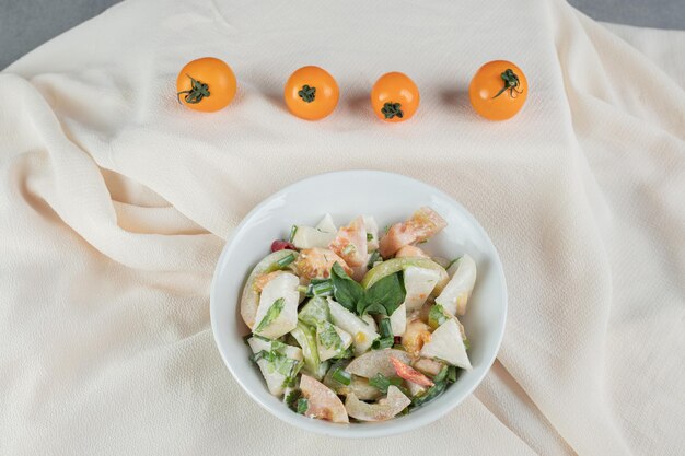 Mixed ingredient seasonal salad with vegetables and fruits in a white dish.