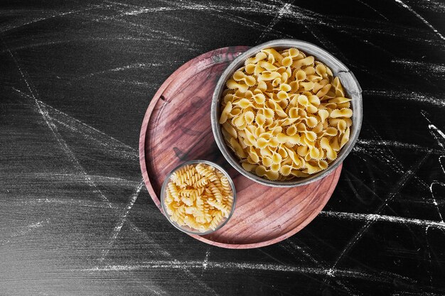 Mixed pastas in metallic cups on a wooden platter. 