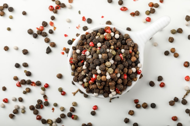 Mixed peppercorns in a white scoop flat lay on spicy and white background