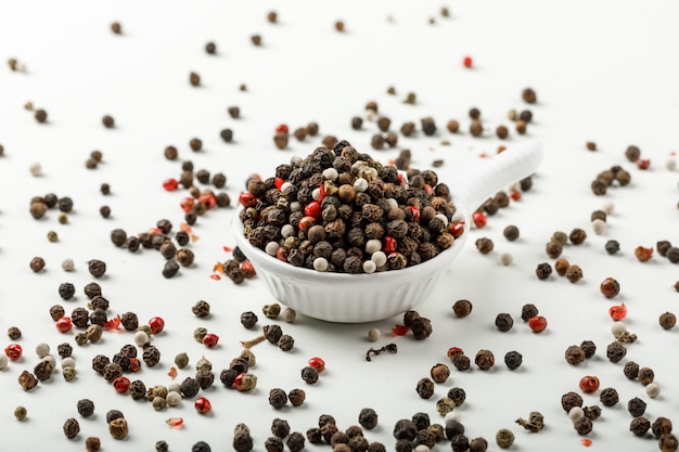 Mixed peppercorns in a white scoop side view on spicy and white background