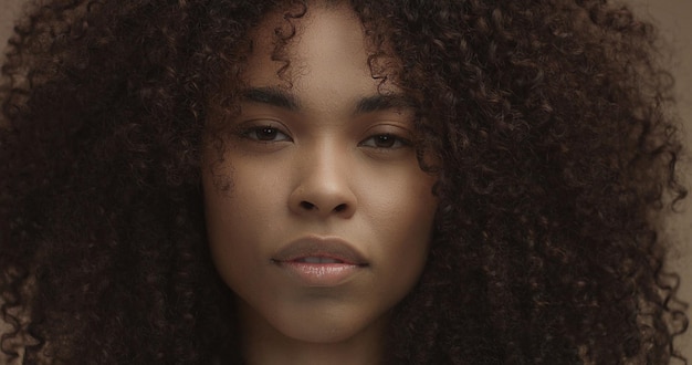 Mixed race black woman portrait with big afro hair curly hair in beige background Face closeup with ideal skin Natural makeup