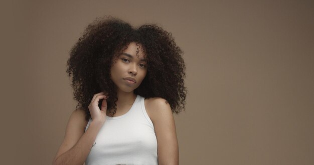 Mixed race black woman portrait with big afro hair curly hair in beige background Touching her hair