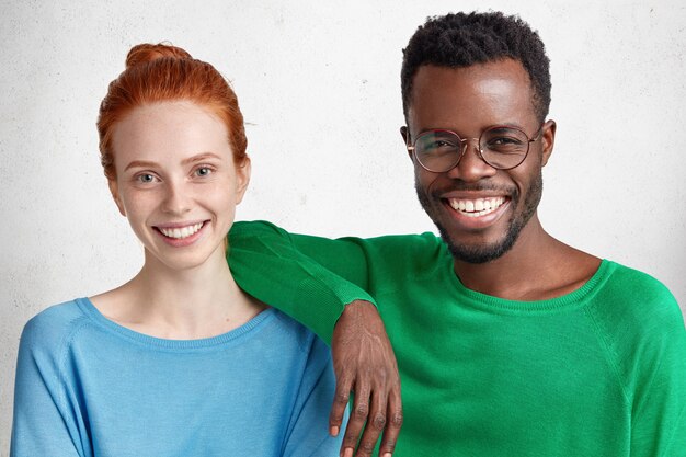 混合人種関係の概念。 Delihghted幸せな黒と白の女性と男性は明るいセーターを着て、白に対して一緒にポーズ