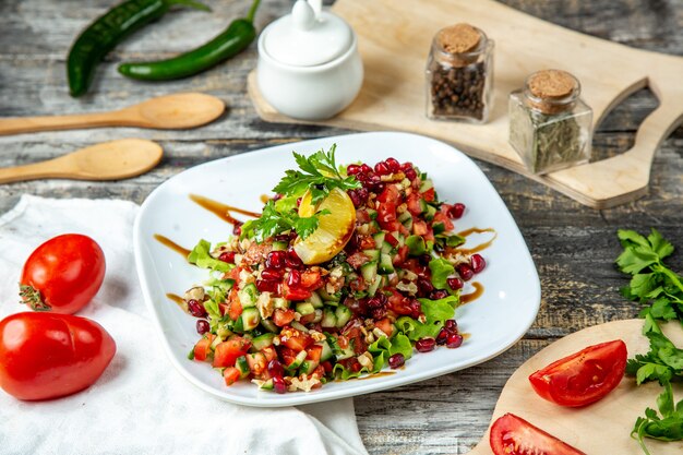 Free photo mixed salad cucumber tomato onion pomegranate lemon side view