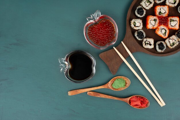 Mixed sushi plate, soy sauce and red caviar on blue surface