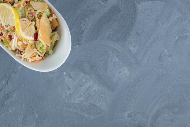 Mixed vegetable salad garnished with lemon slices on marble table.