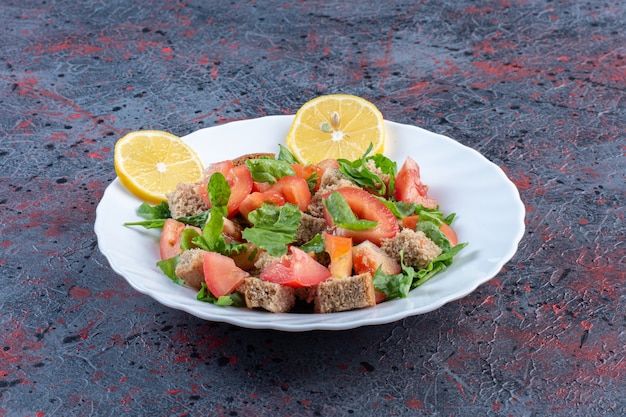 Insalata di verdure miste con contorno di limone e crosta secca sulla tavola nera.