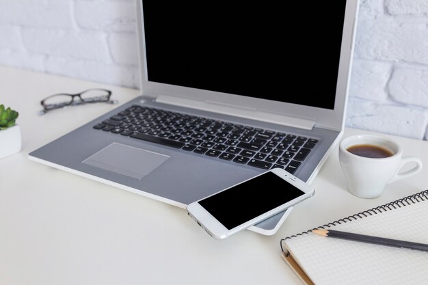 Mobile phone on the laptop with coffee cup on white desk