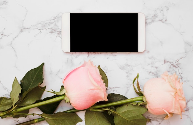 Mobile phone with two pink roses on marble backdrop