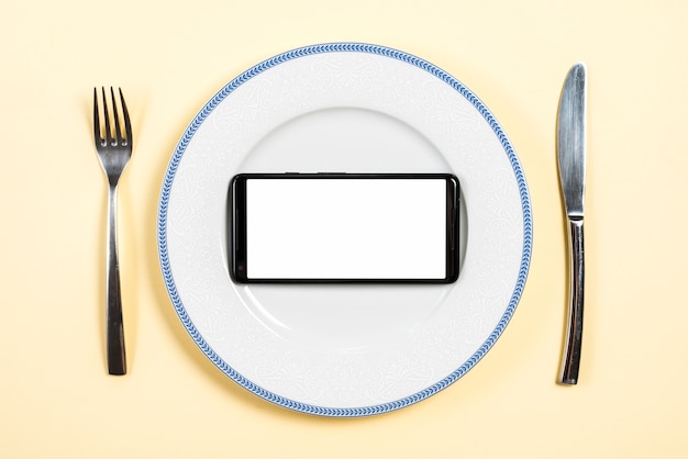 베이지 색 배경 포크와 버터 나이프와 함께 접시에 흰색 화면 디스플레이와 휴대 전화