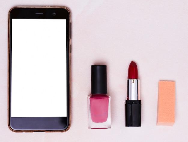 Mobile phone with white screen; nail varnish bottle; red lipstick and adhesive notes on colored backdrop