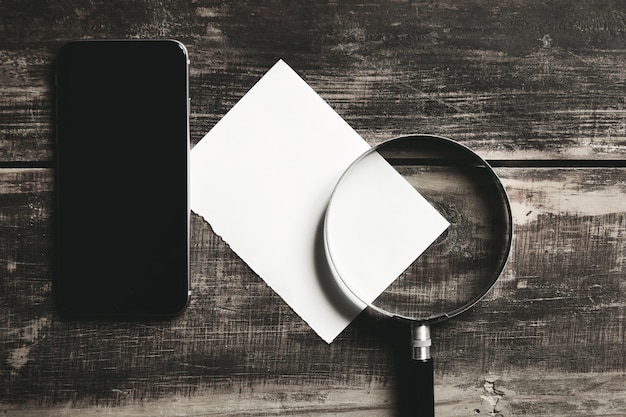 Free photo mobile smartphone, magnifier and sheet of white paper isolated on black farm wooden table