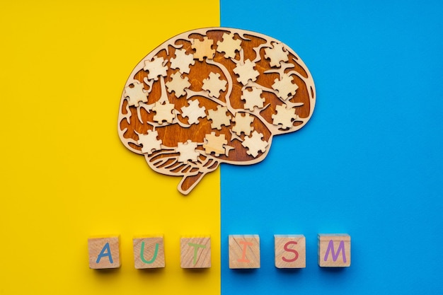 Mock up of a human brain with scattered puzzle pieces on a yellow and blue background. six cubes with the inscription autism.