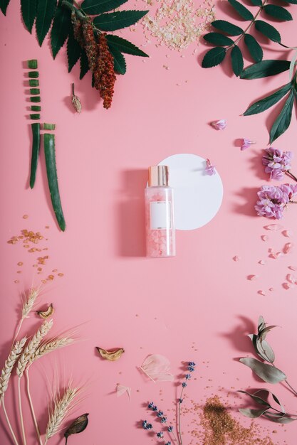 Mockup of bottle in flowers on pink wall with white circle shape. Spring wall with spa composition. Flat lay